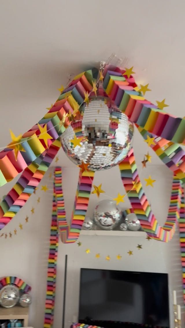 Rainbow pleated paper garlands and gold stars surrounding a mirrored disco ball.