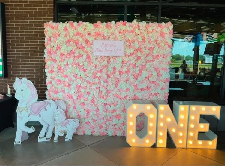 Pink and white floral wall with illuminated ONE letters and horse cutouts.