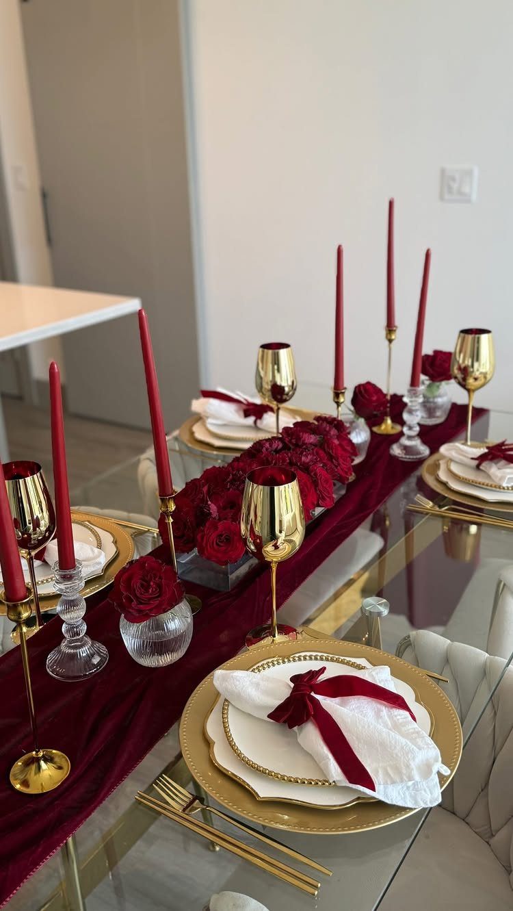 Elegant dining table set with red velvet runner, gold plates, and red roses.