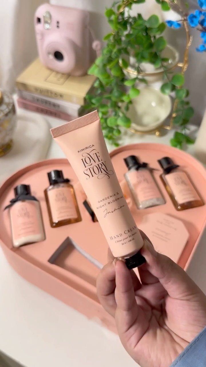 Hand holding a peach hand cream tube over a heart-shaped beauty gift set