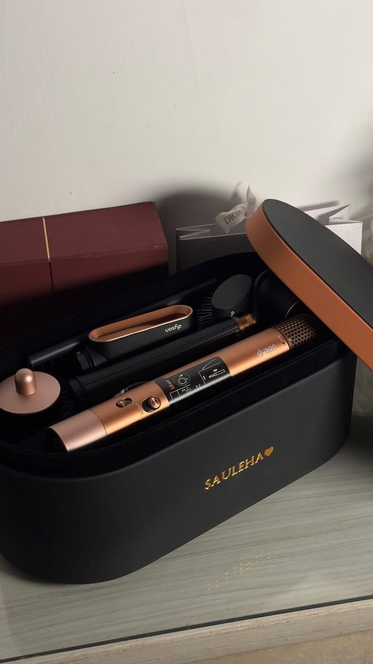 Hair styling tools in a black storage case with gold lettering on a shelf.