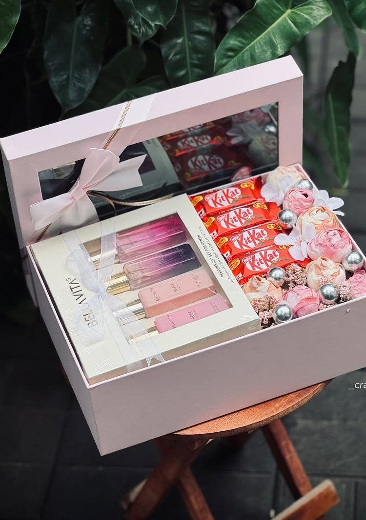 Pink gift box containing perfumes, KitKat chocolates, and artificial roses on a stool