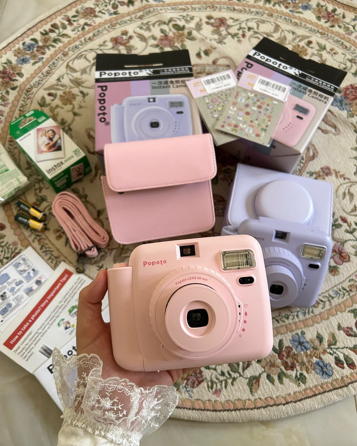 Pink digital camera held in hand surrounded by camera accessories on a rug