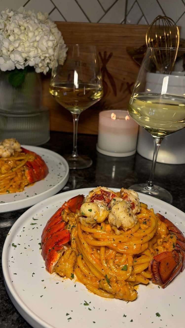 Lobster pasta plates and white wine glasses with white flowers and a candle.