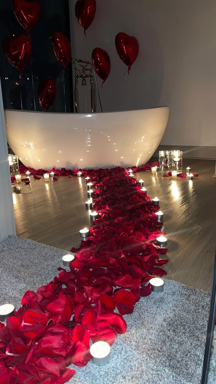 White bathtub with a path of red rose petals and glowing tea light candles.