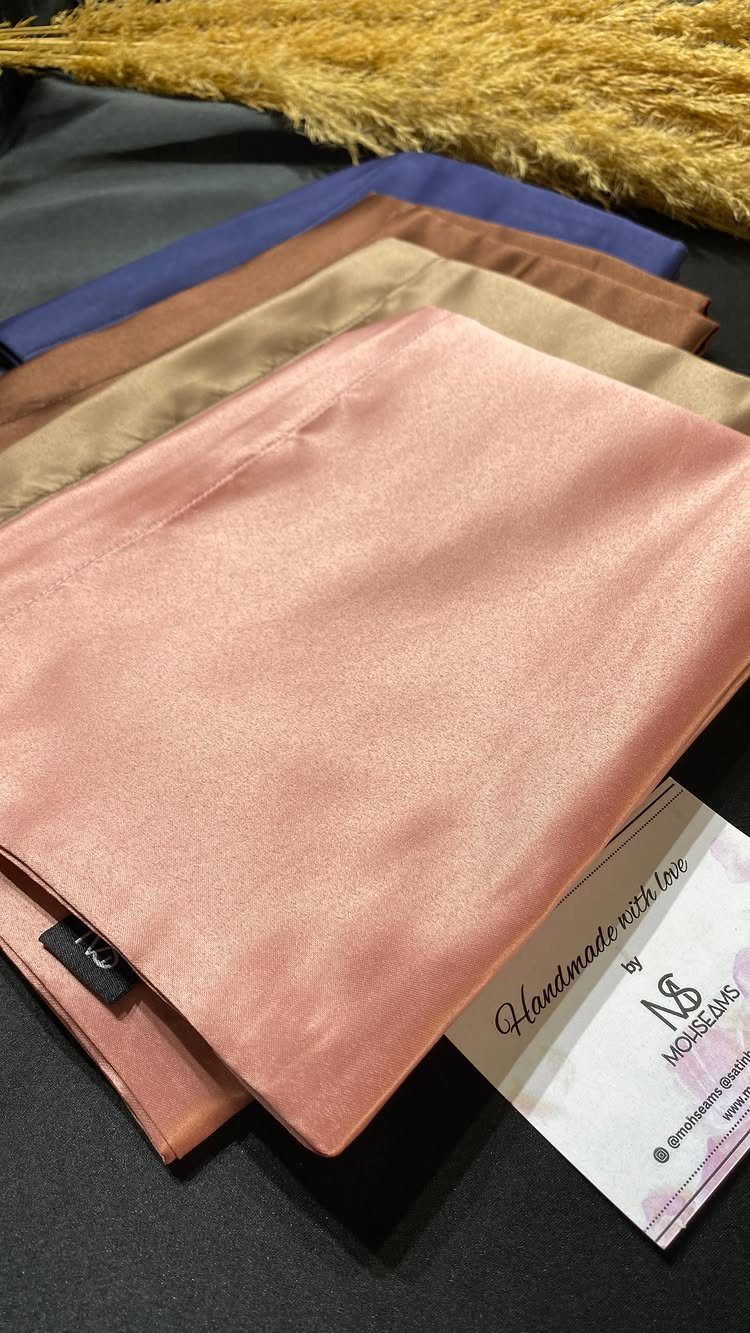 Satin pillowcases in various colors stacked next to a business card and pampas grass.