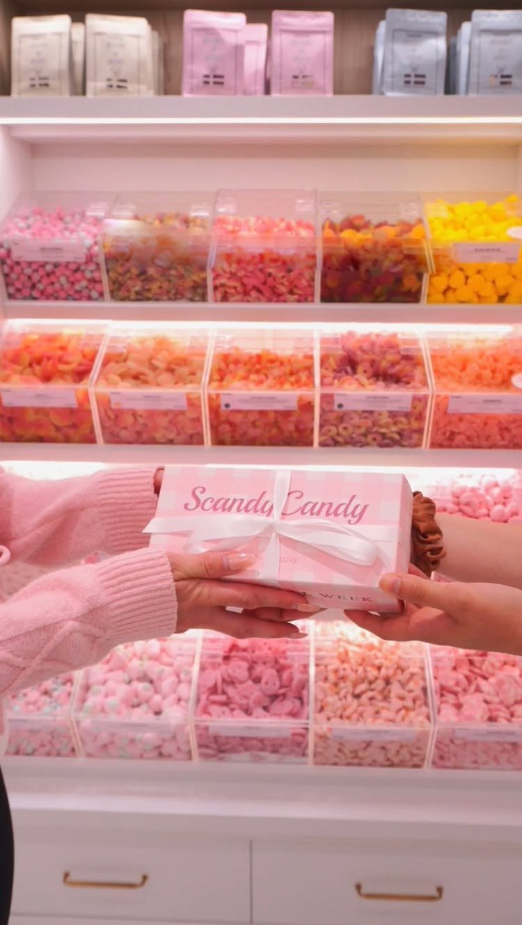 White Scandy Candy gift box held in front of colorful candy store shelves.