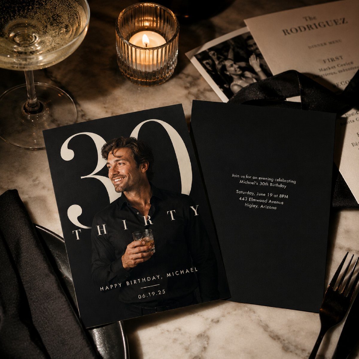 Black 30th birthday invitation card with man's photo on a marble dinner table