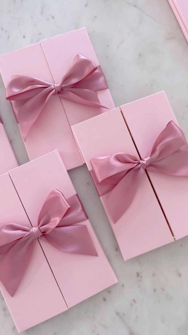 Pink invitation cards tied with satin bows on a white marble background