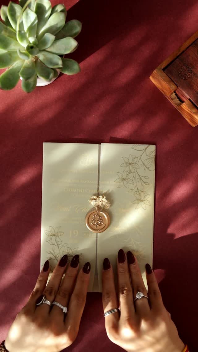 Cream invitation card with gold wax seal held by hands with dark nails