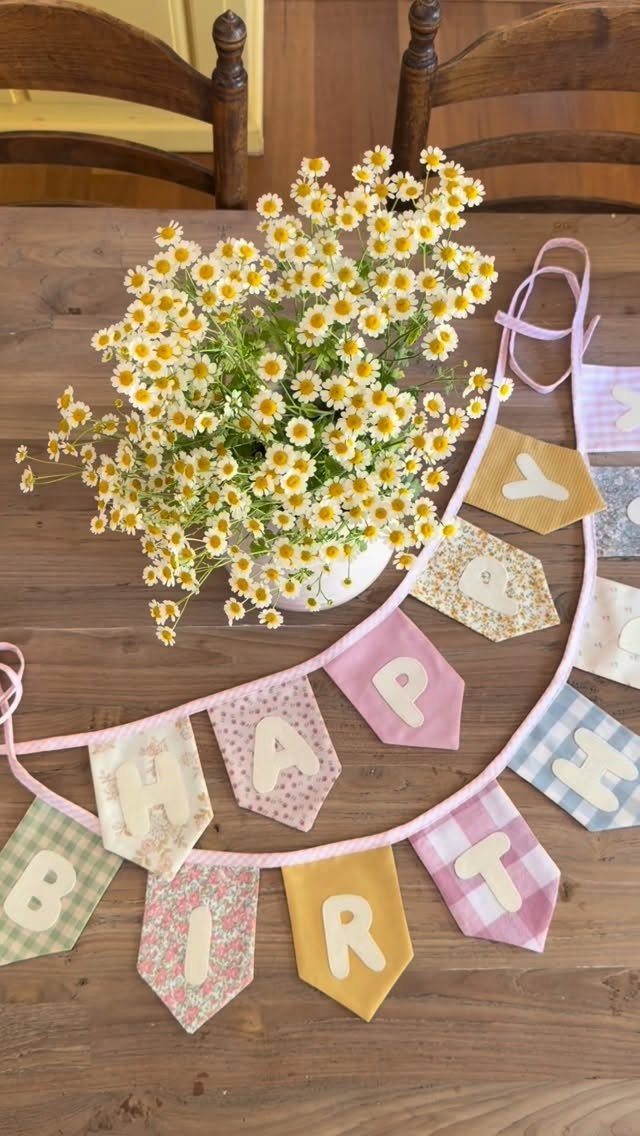 Fabric bunting banner spelling Happy Birthday next to yellow daisies on wooden table