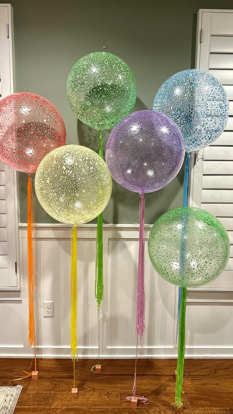 Transparent confetti balloons in various colors with matching streamers anchored to a floor.