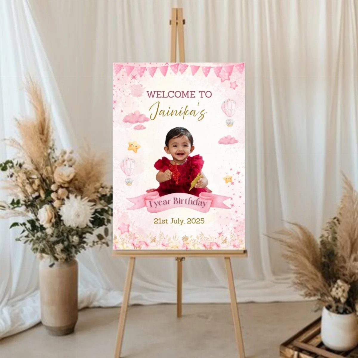 Personalized pink birthday welcome sign on a wooden easel with dried flower arrangements.