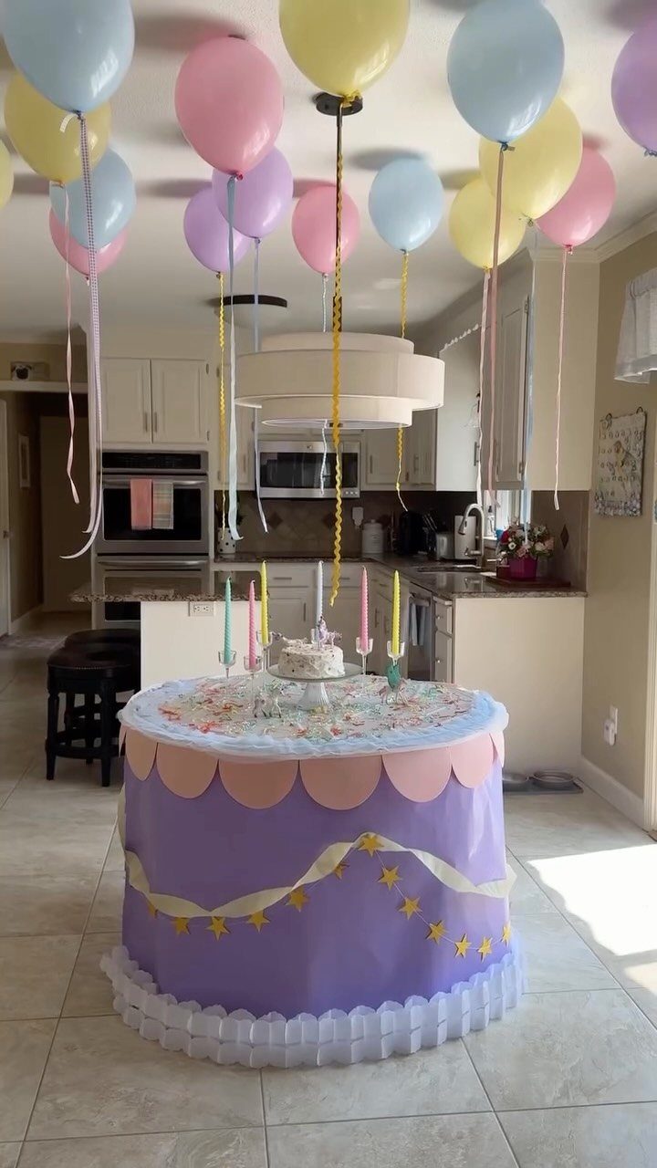 Round purple dessert table with a small cake and floating pastel balloons.