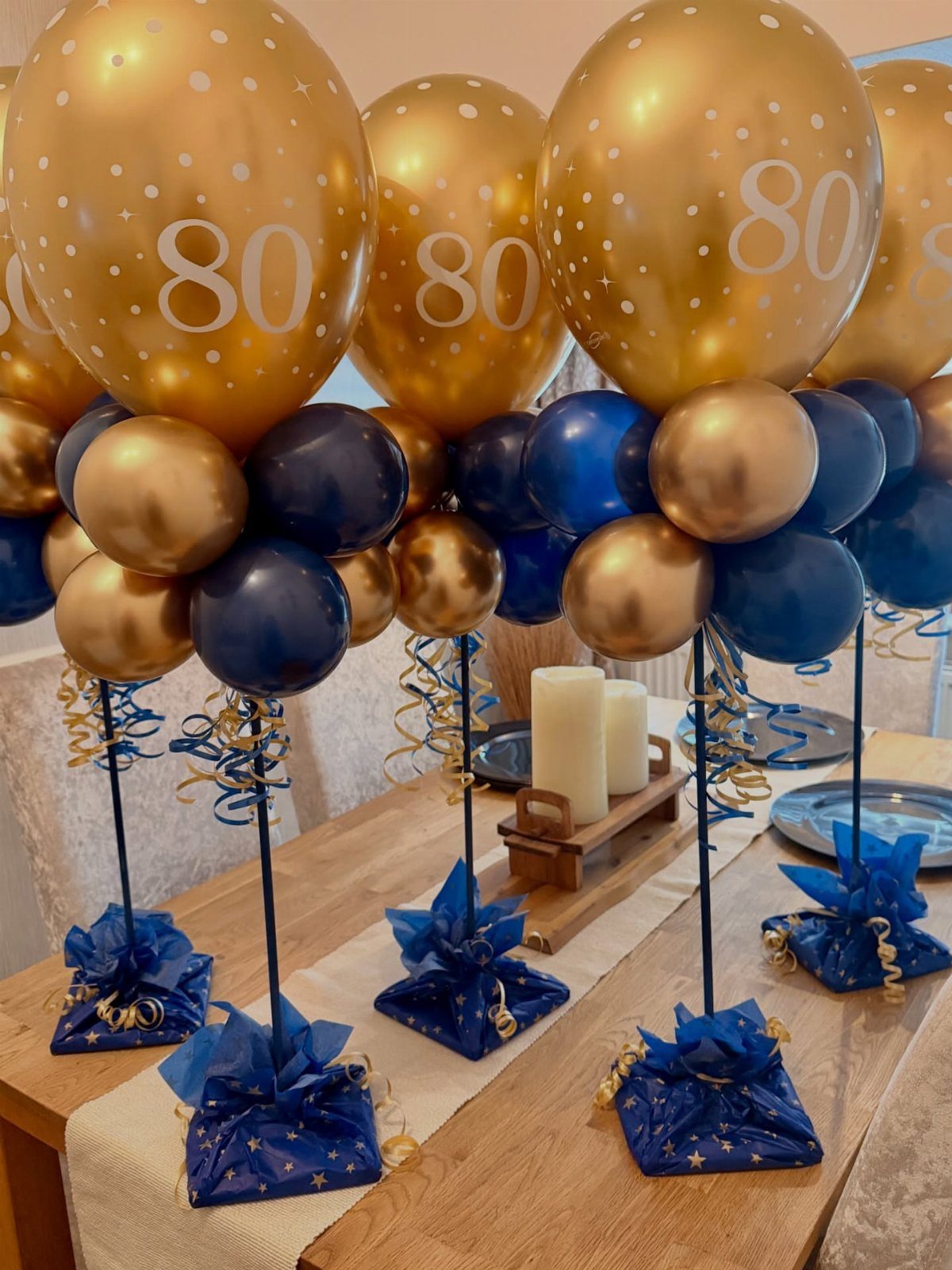 Gold and navy blue balloon centerpieces with number 80 on a wooden table.