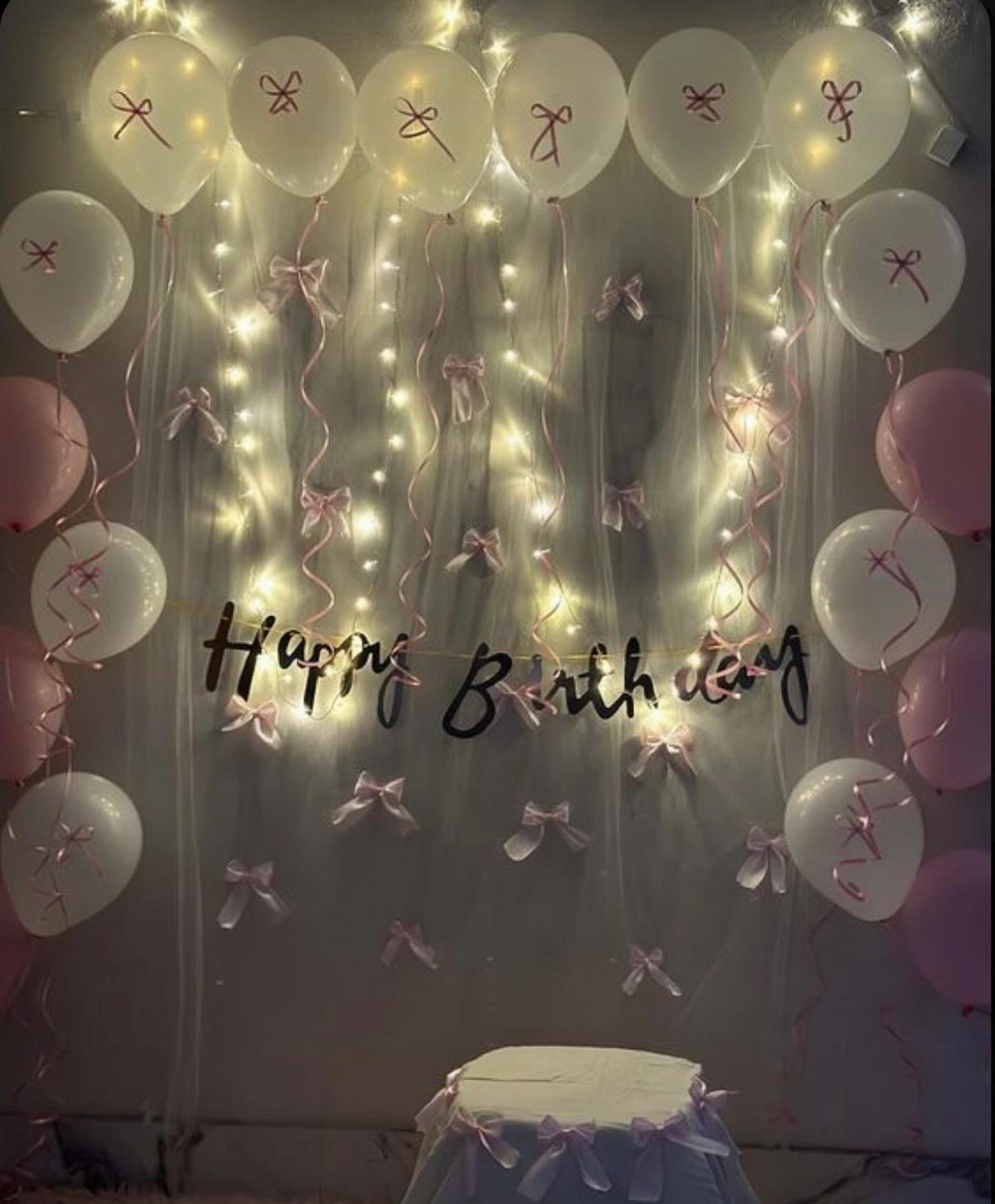 Birthday party decoration with white and pink balloons, fairy lights, and Happy Birthday sign.