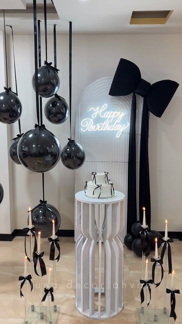 Birthday party decoration with black balloons, white cake, and neon Happy Birthday sign.