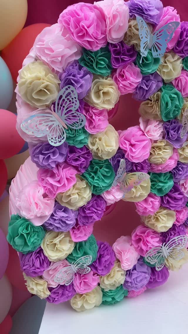 Number eight sculpture covered in pink, purple, and green paper flowers with butterflies.