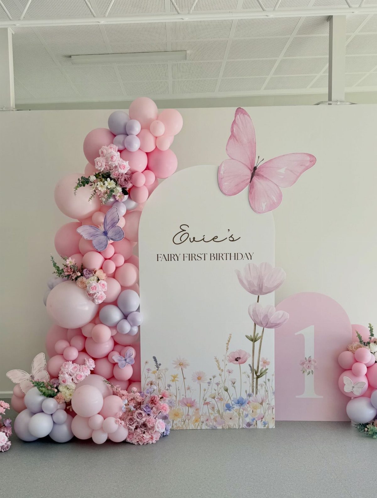 Birthday backdrop with pink and purple balloons, floral accents, and a butterfly panel.