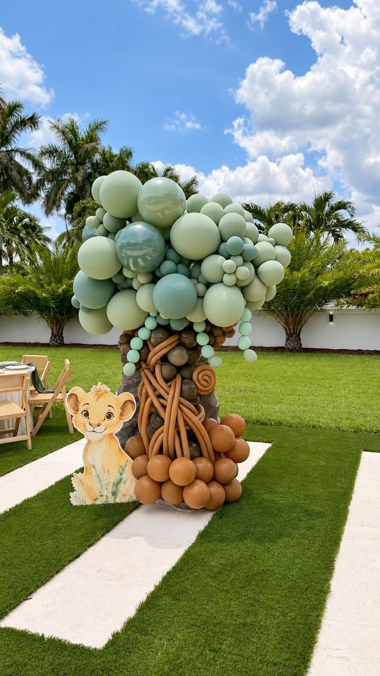 Lion King themed balloon tree decoration with green canopy and brown trunk outdoors.
