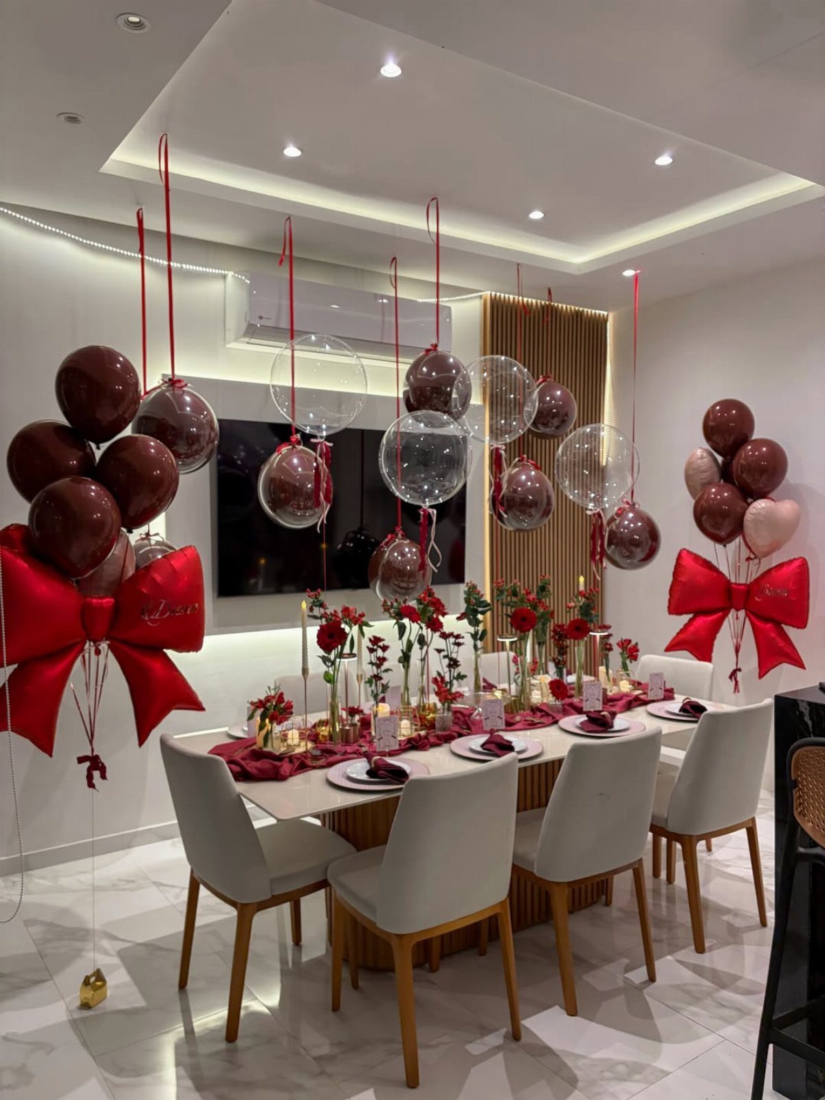 Dining table decorated with red roses, candles, and red tableware surrounded by balloons.