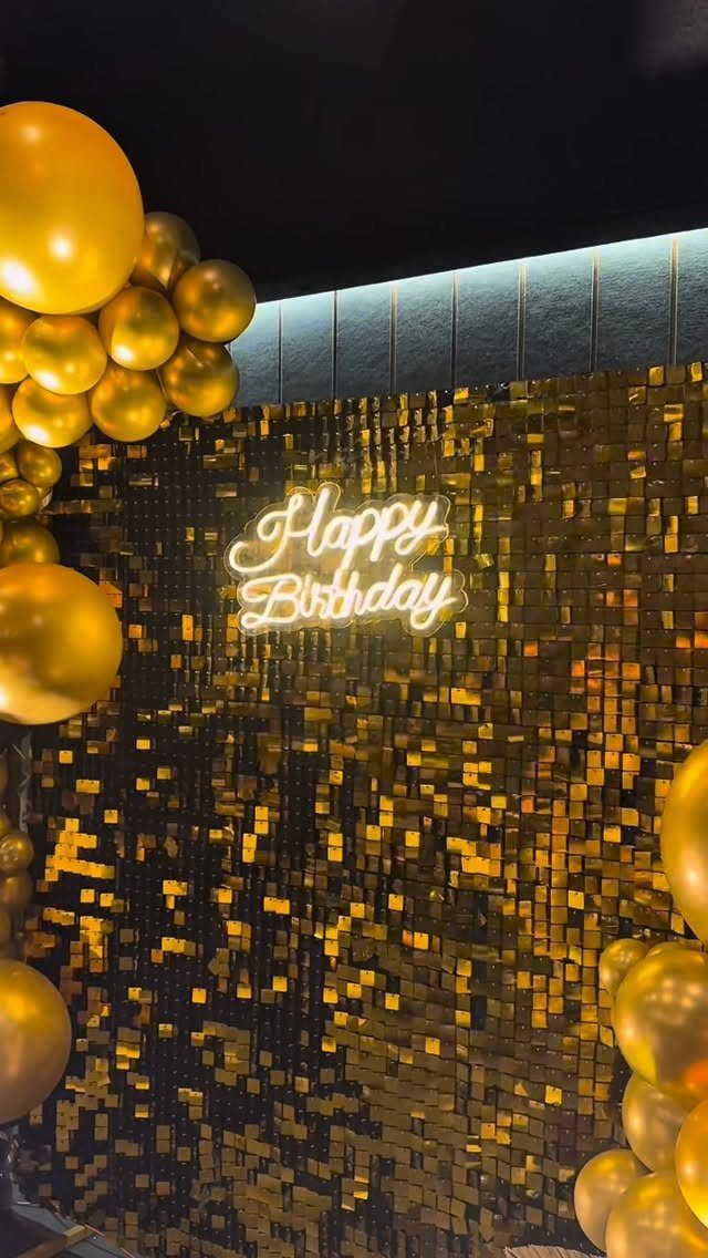Gold sequin backdrop with neon Happy Birthday sign and gold balloon arches.