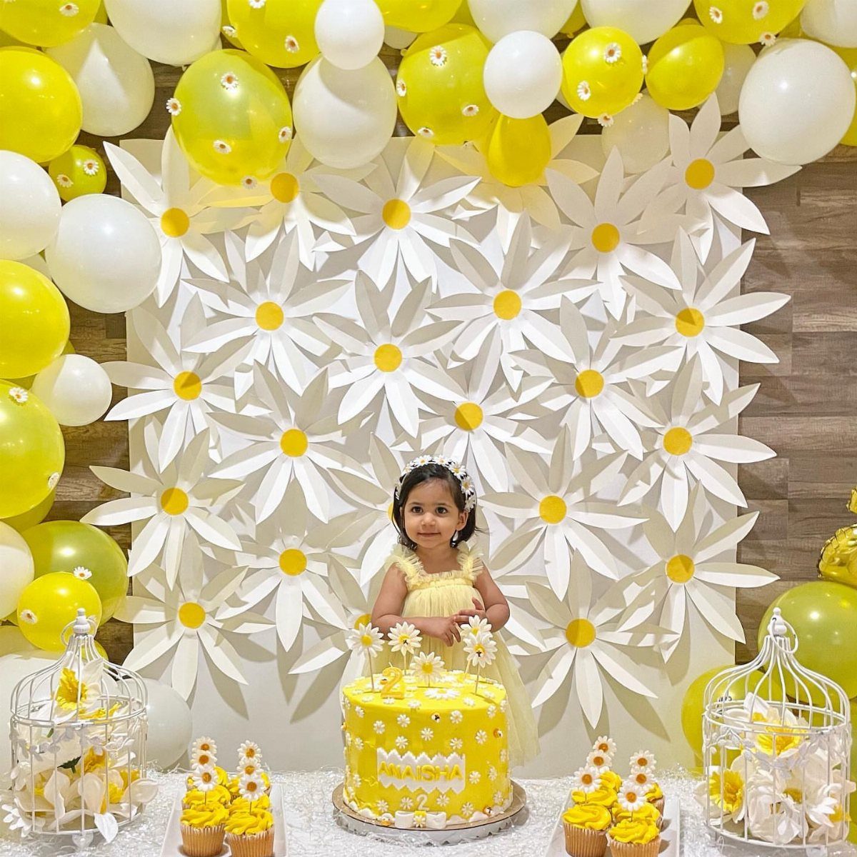 Young girl in yellow dress standing before a white paper flower wall backdrop.