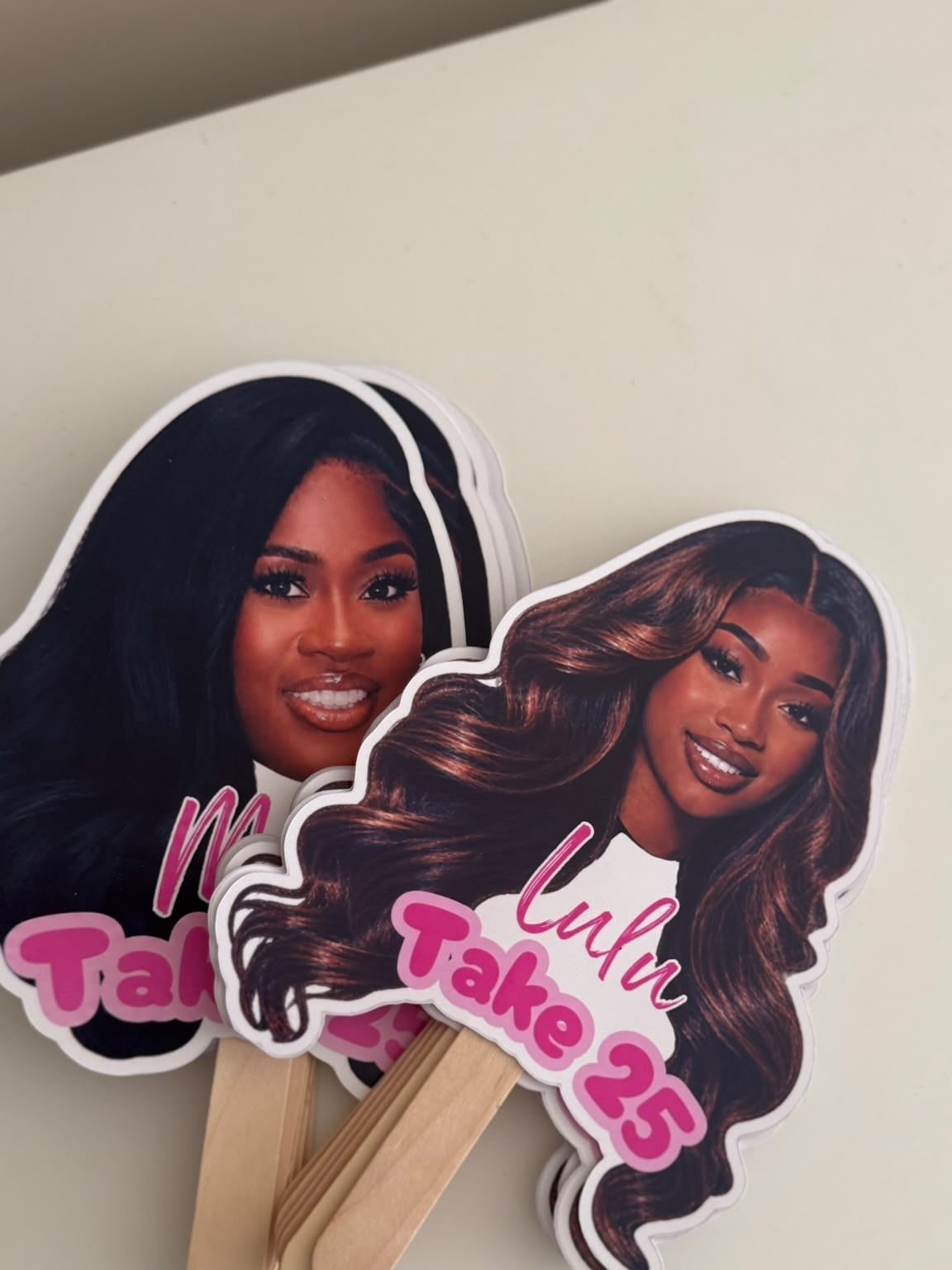 Custom cardboard face cutouts of a woman with pink birthday text on sticks.