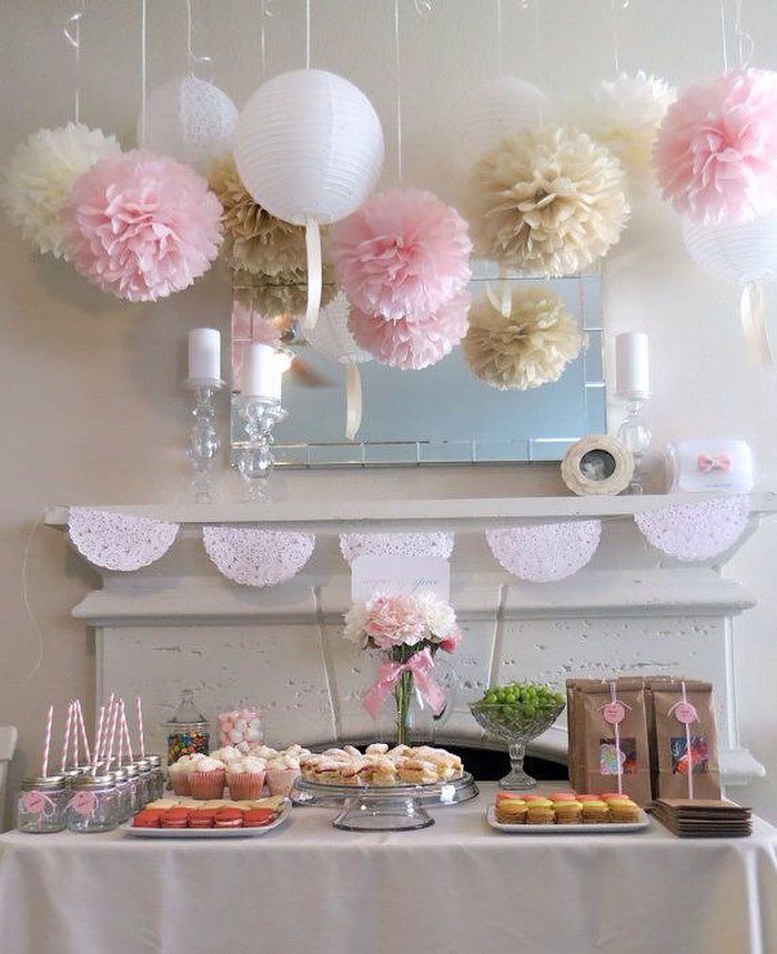 Tissue paper pom-poms and lanterns hanging above a decorated birthday dessert table.