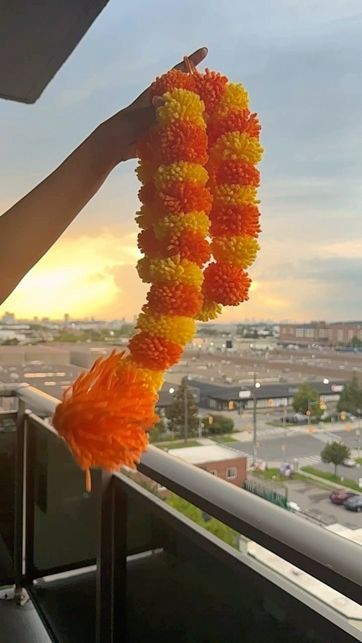 Orange and yellow yarn pom-pom garland held against a city sunset background.