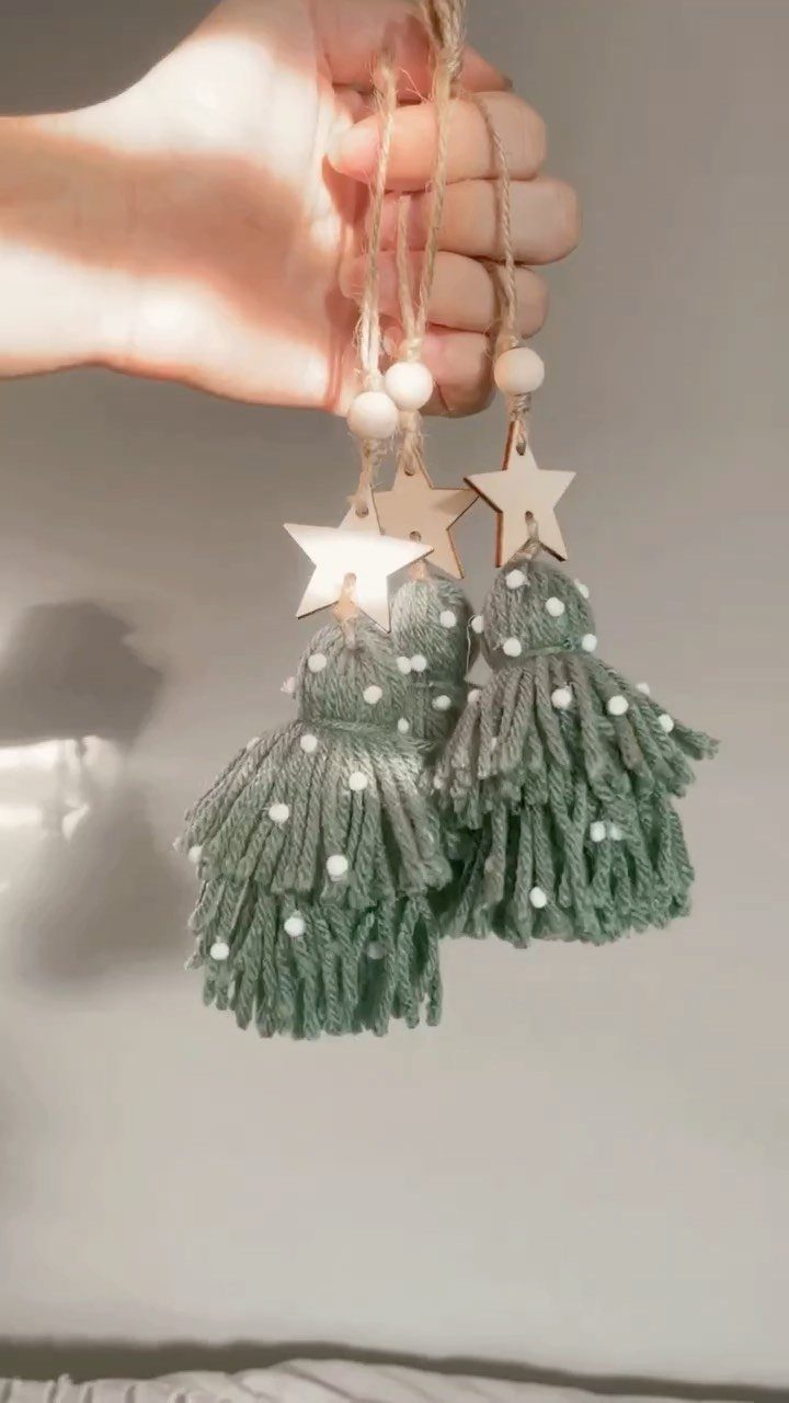 Hand holding three sage green yarn tassels with wooden stars and beads.