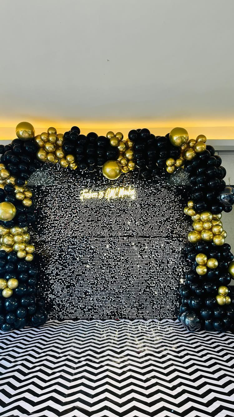 Black and gold balloon arch framing a shimmering black sequin party backdrop.
