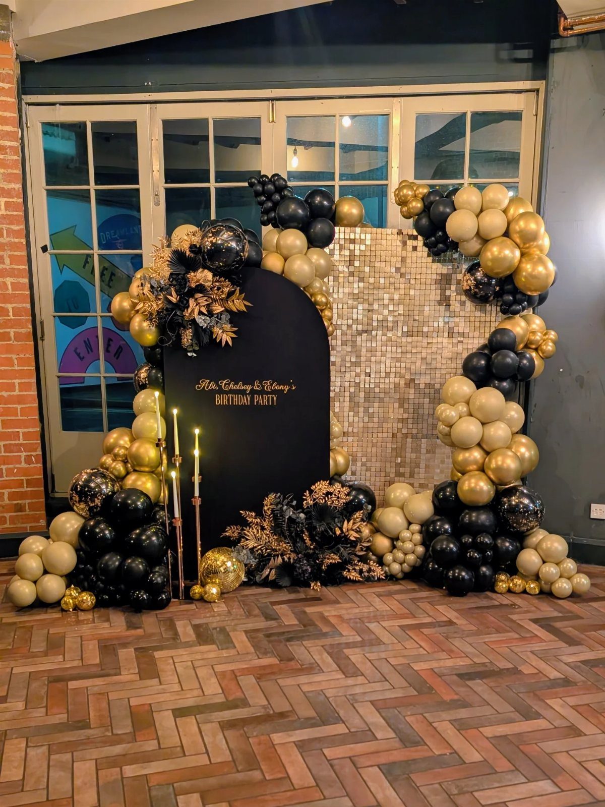 Black arched backdrop with gold and black balloons and shimmering gold sequin wall.