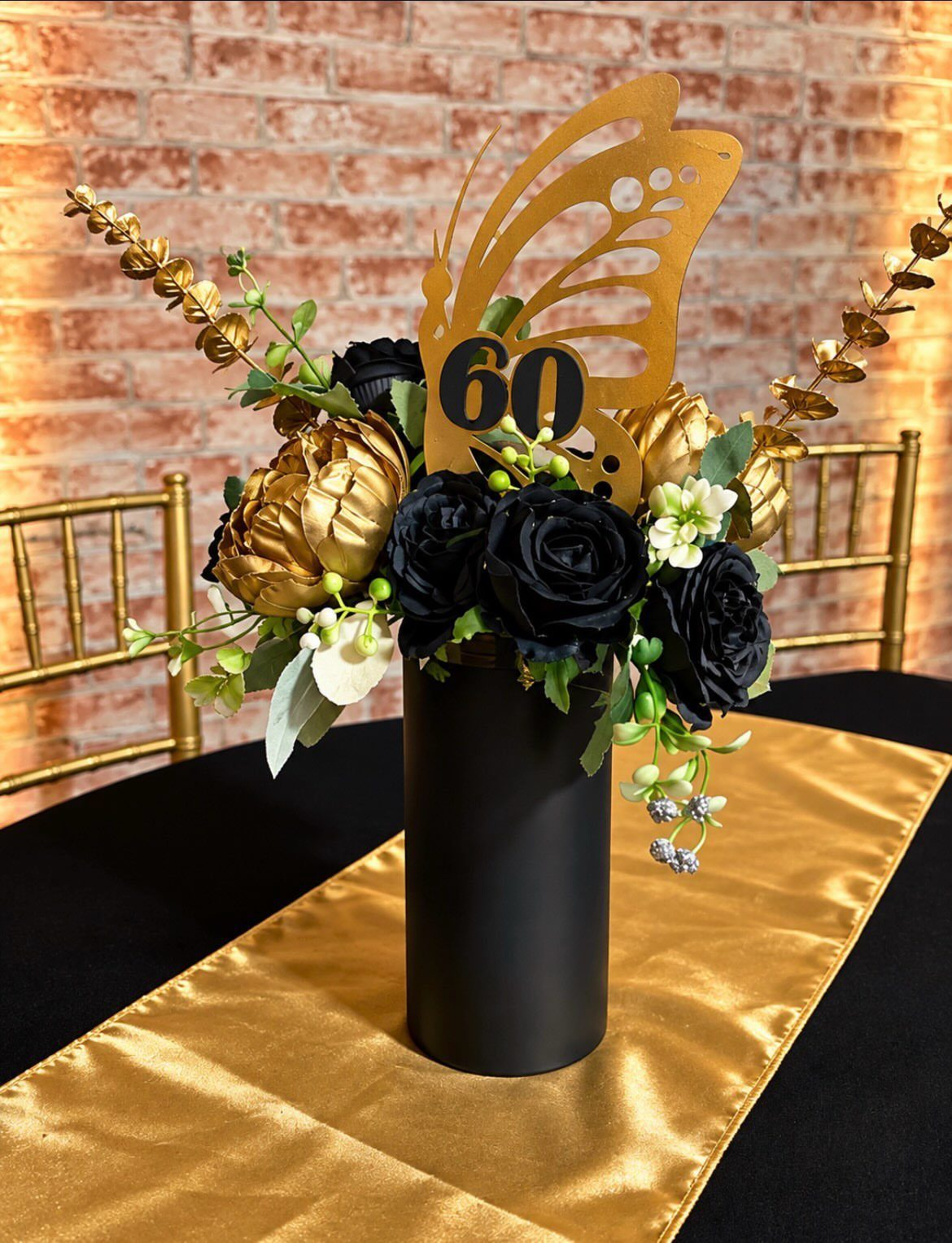 Black and gold floral centerpiece with a butterfly topper on a gold runner.