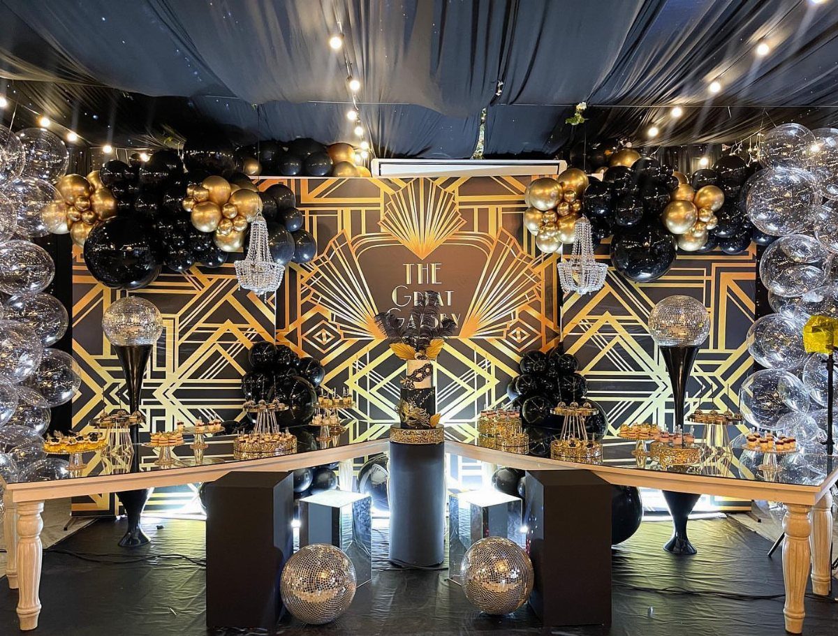 Gatsby-inspired party decor with black and gold Art Deco backdrop and balloon arches.