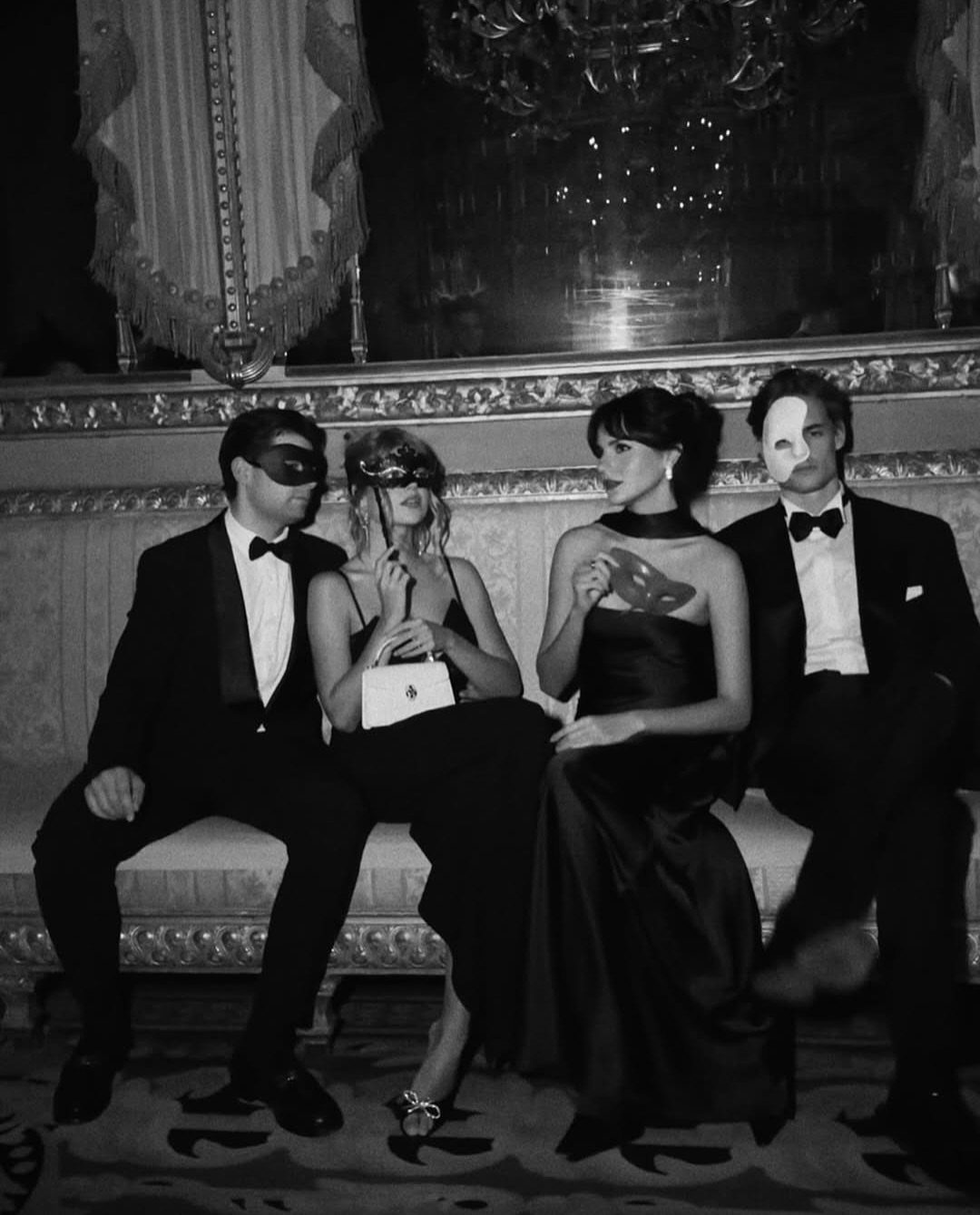 Four people in formal black and white attire and masks sitting on a sofa.