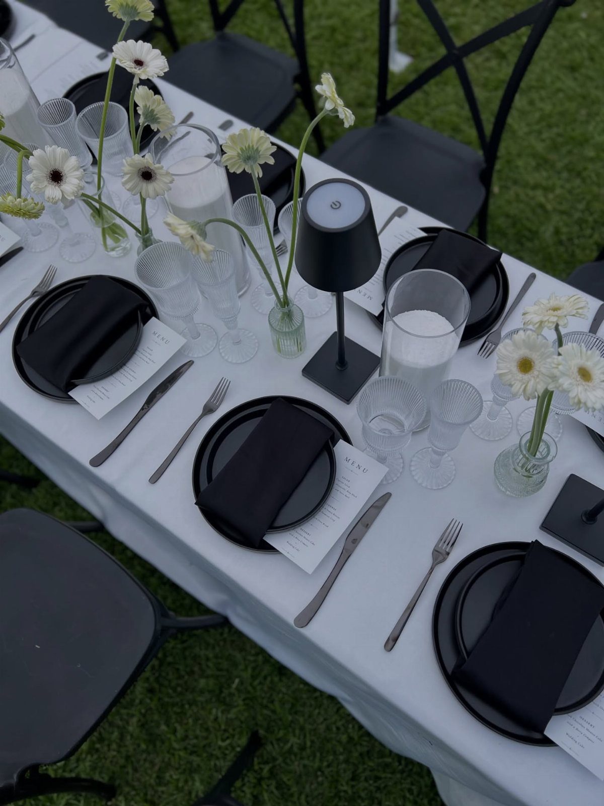 Outdoor dining table set with black plates and white daisies on white tablecloth