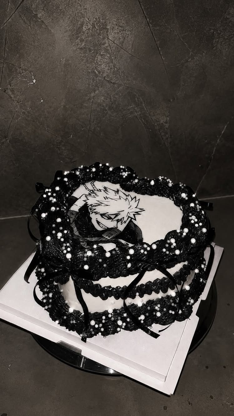 Two-tier white cake with black frosting decorations and an anime character image.