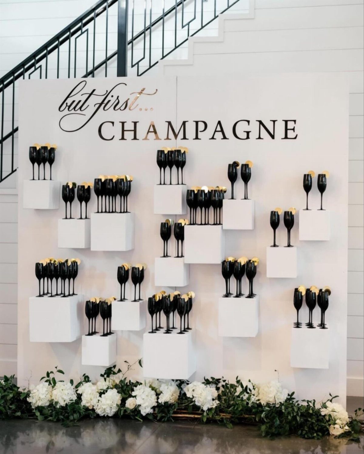 Black champagne flutes on white shelves with champagne text and white floral arrangements