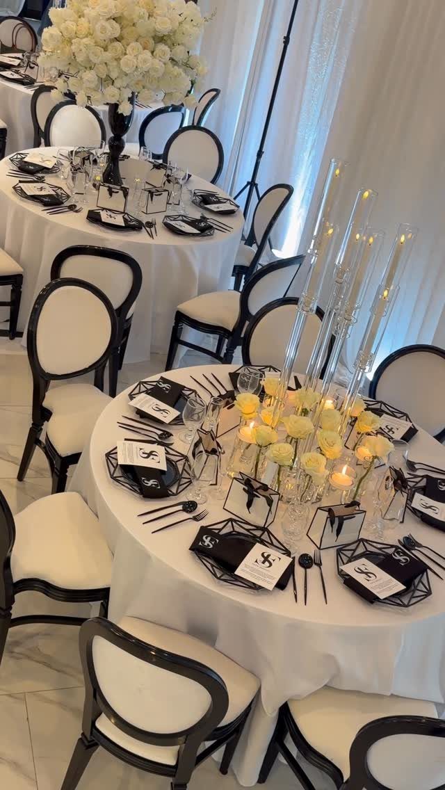 Round tables with white linens, black plates, and white floral centerpieces for a party.