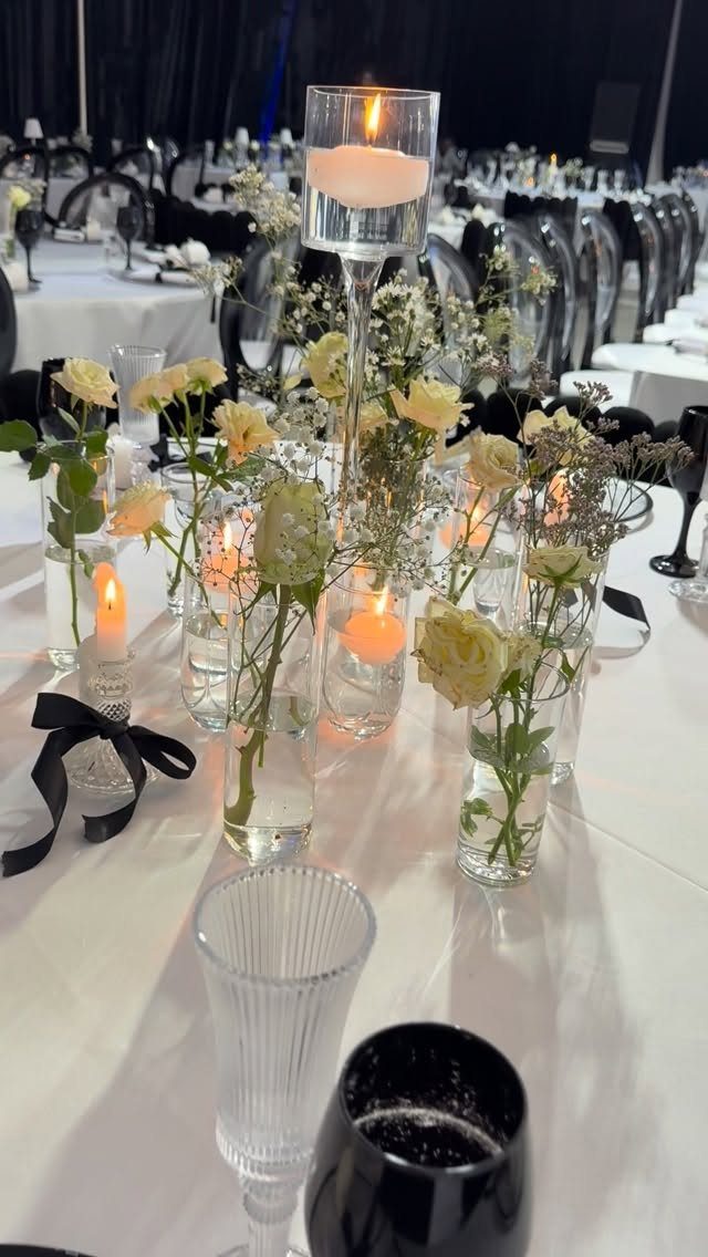 White roses and floating candles on a white tablecloth with black chairs behind.