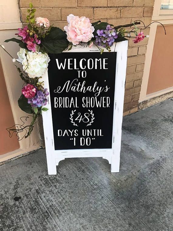 Black chalkboard welcome sign with floral decorations counting down days until the wedding.