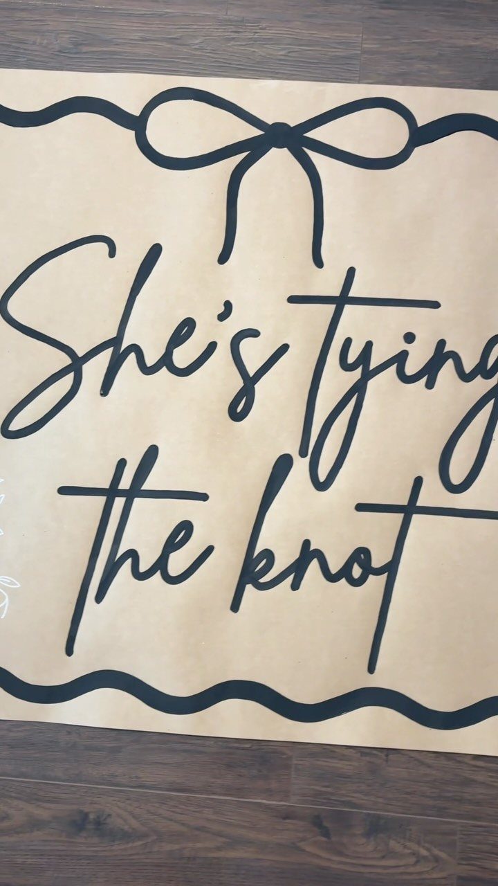 Tan welcome sign with black text saying She's tying the knot on wood floor