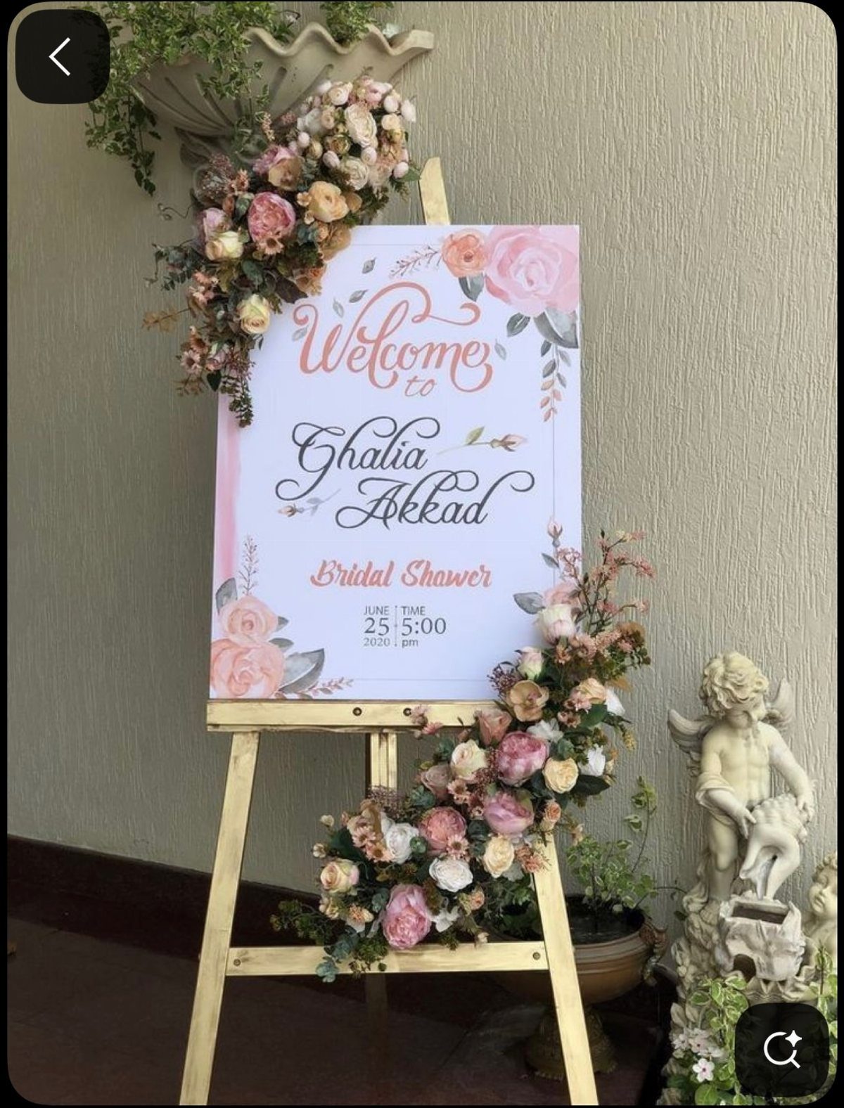 Bridal shower welcome sign on a wooden easel adorned with pink floral arrangements.