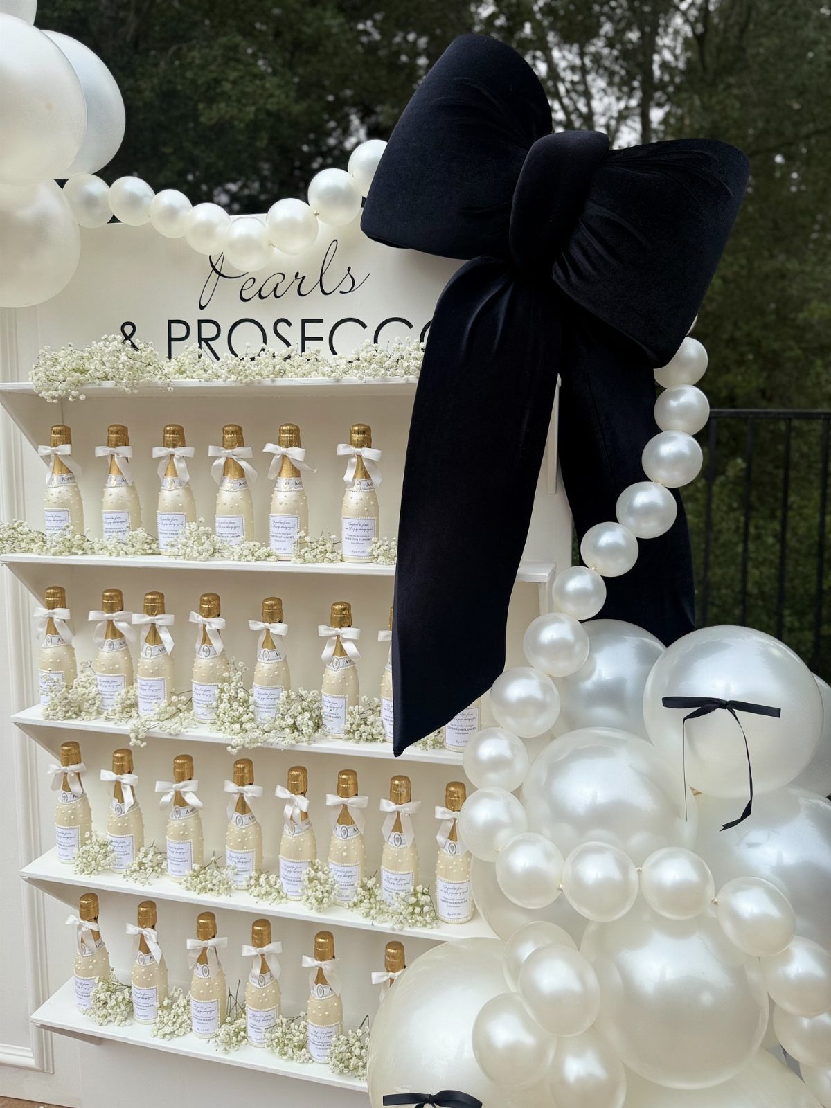 Pearls and Prosecco sign above a shelf of mini champagne bottles and balloons