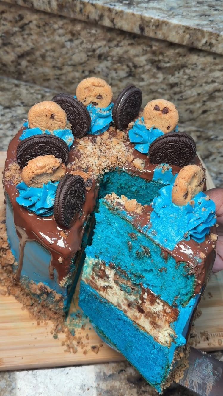 Blue layered cake topped with chocolate chip and sandwich cookies and chocolate ganache
