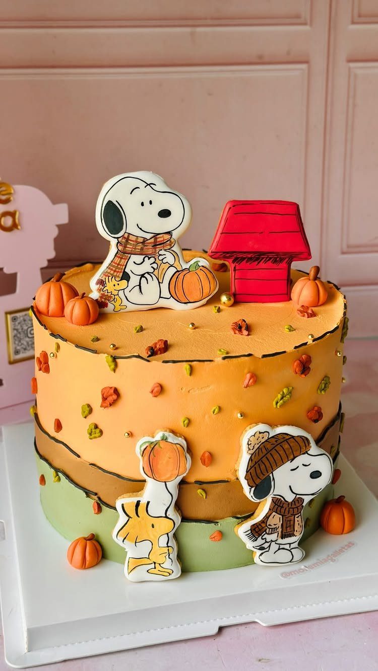 Orange and green cake decorated with Snoopy cookies, pumpkins, and autumn leaves.