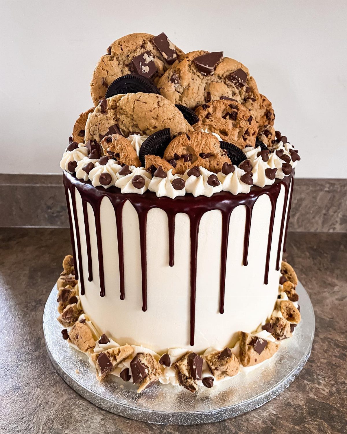 White frosted cake topped with chocolate chip and Oreo cookies and chocolate drip.