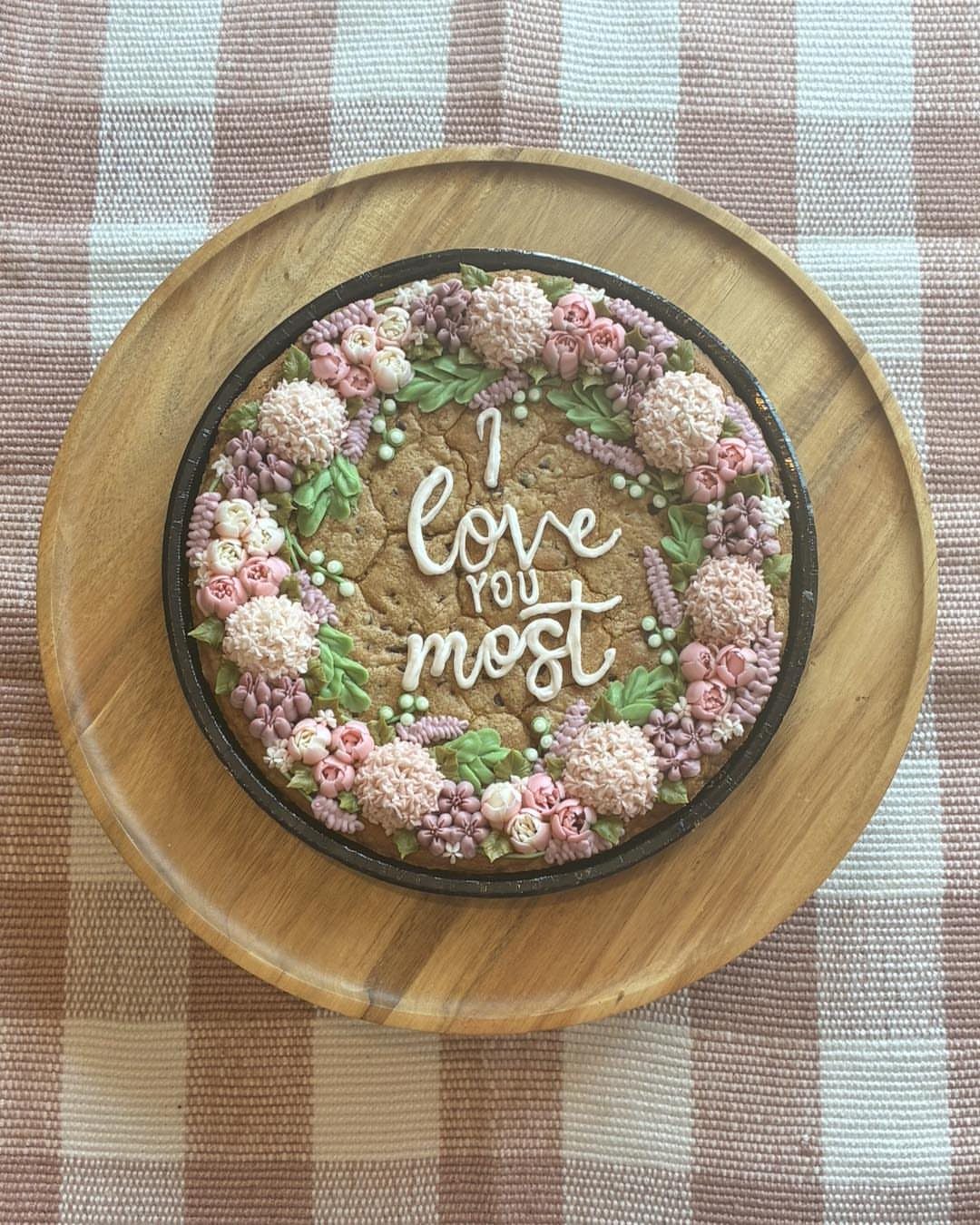 Cookie cake decorated with a buttercream flower wreath and white icing text.