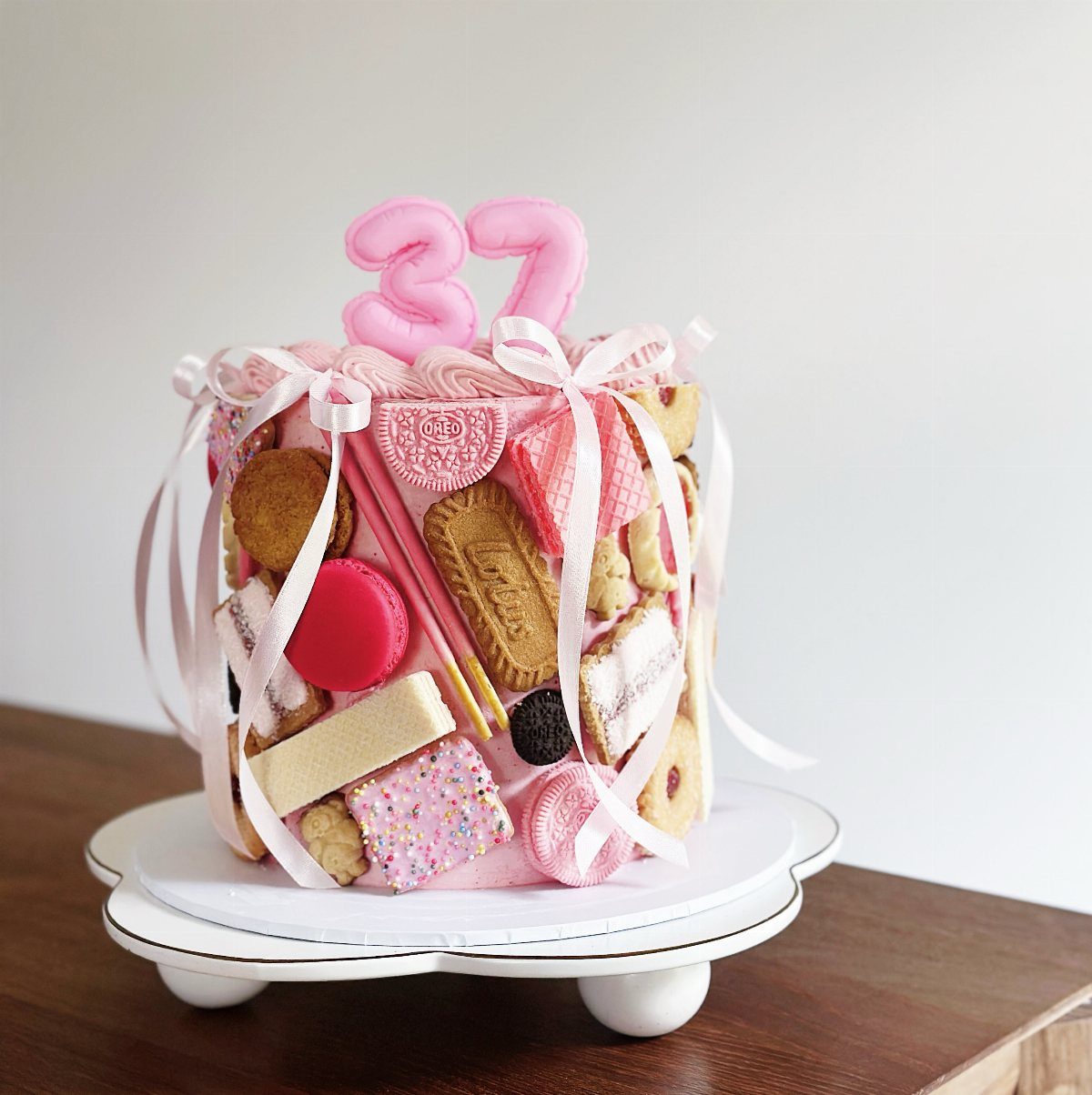 Pink frosted cake decorated with various cookies and macarons with a number 37 topper